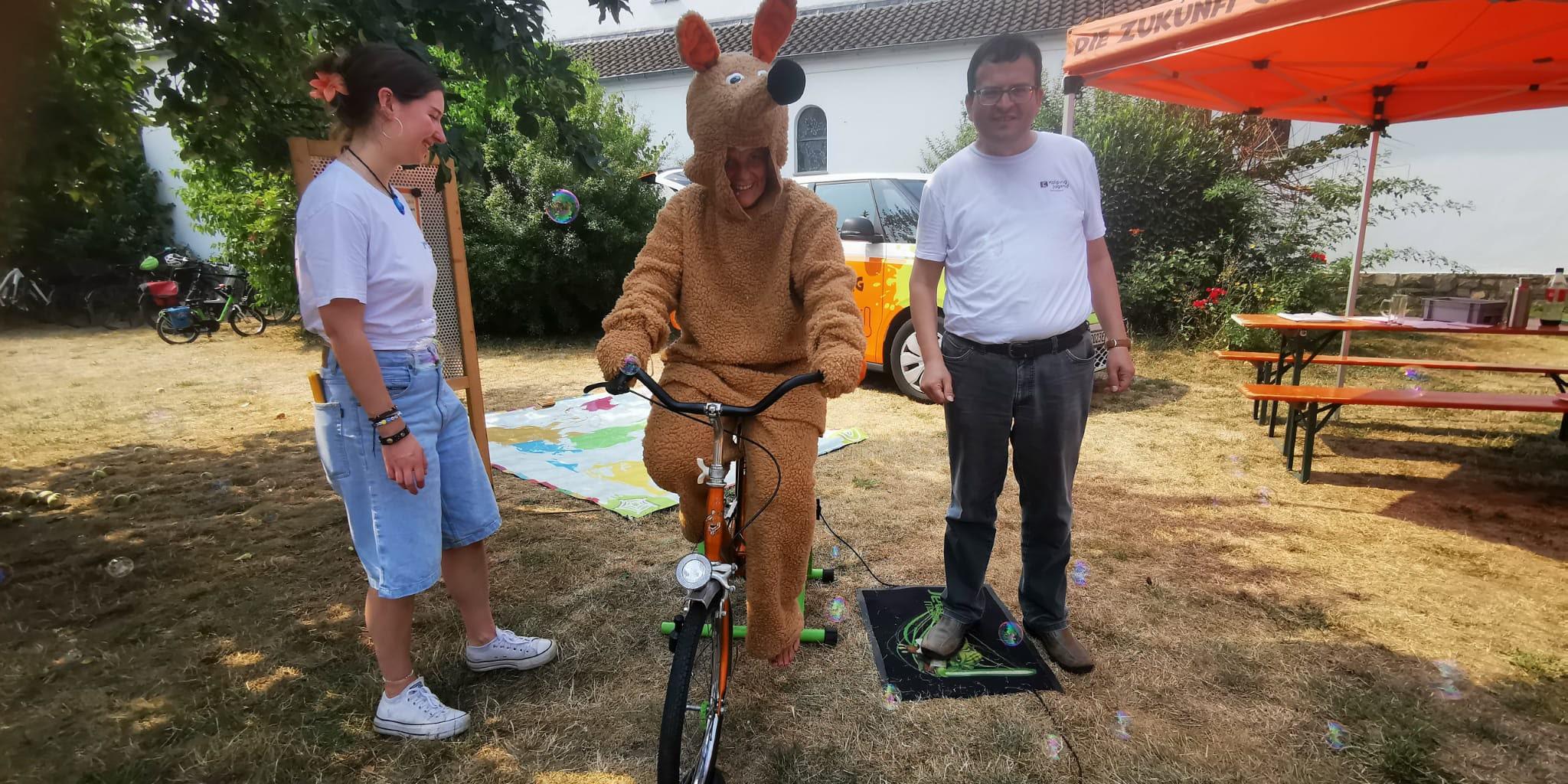 Schnuffi das Maskotchen auf dem Fahrrad, dazu zwei ehrenamtliche Mitarbeiter (c) Kolpingsfamilie Arheilgen Schnuffi das Maskotchen auf dem Fahrrad, dazu zwei ehrenamtliche Mitarbeiter
