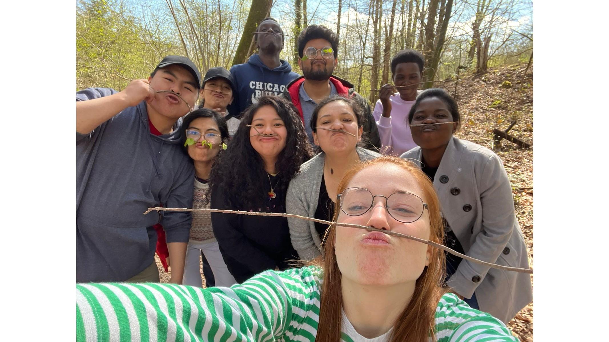Junge Menschen posieren fröhlich für ein Selfie und balancieren dabei einen Zweig zwischen Oberlippe und Nase.